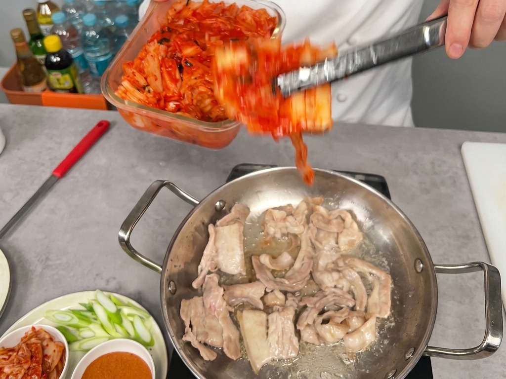 삼겹살이 담긴 팬에 신김치를 넣는 모습