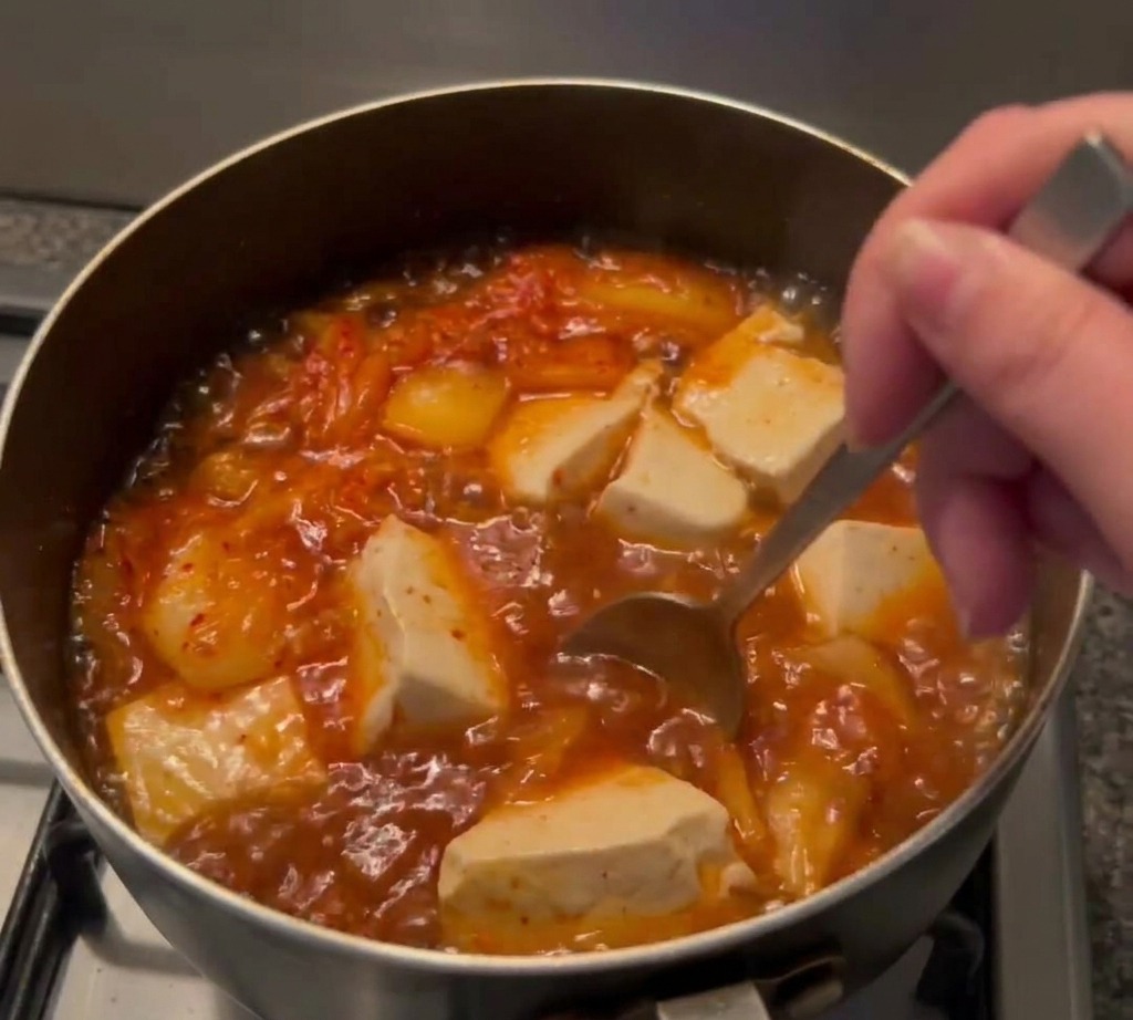 김치와 순두부가 담긴 끓는 찌개에 숟가락으로 양념을 섞는 모습