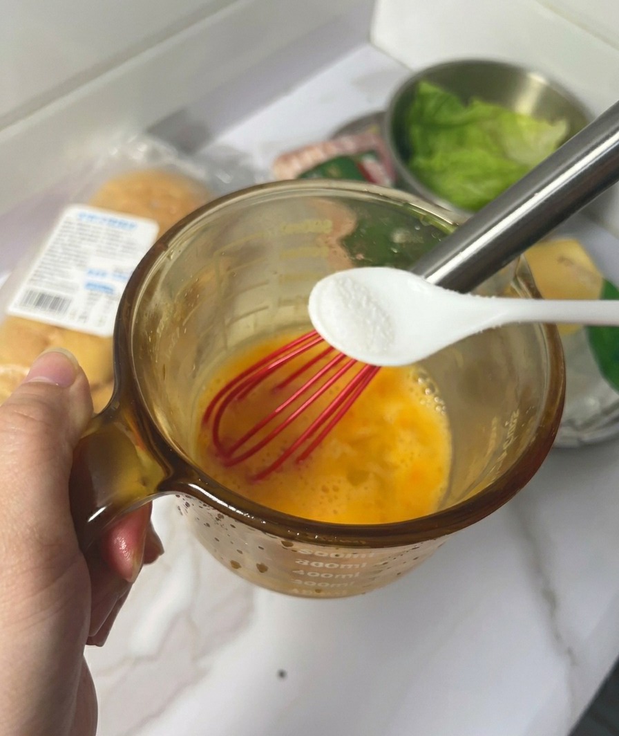 거품기로 달걀을 섞으며 작은 스푼으로 소금을 넣는 모습