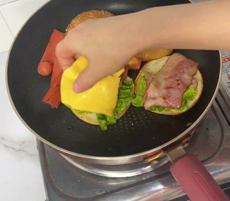 베이컨 위에 노란색 체다 치즈를 한 장 올리는 모습