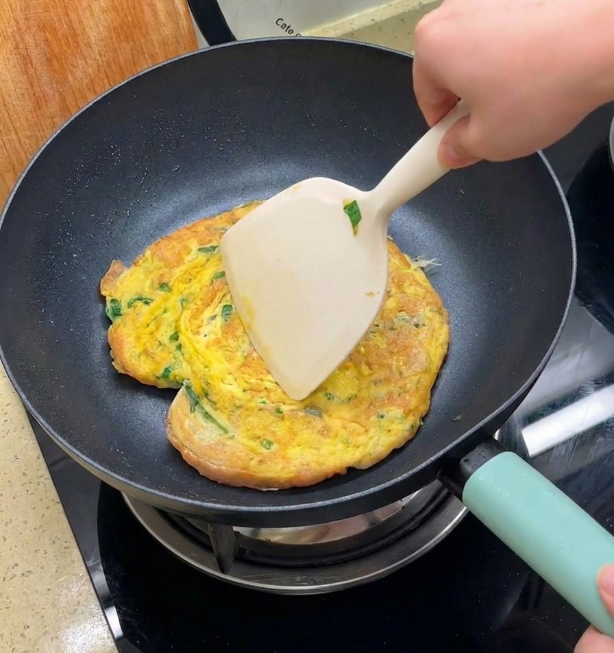넓은 뒤집개로 프라이팬 속의 노릇한 오믈렛과 버거 번을 한꺼번에 뒤집는 모습.