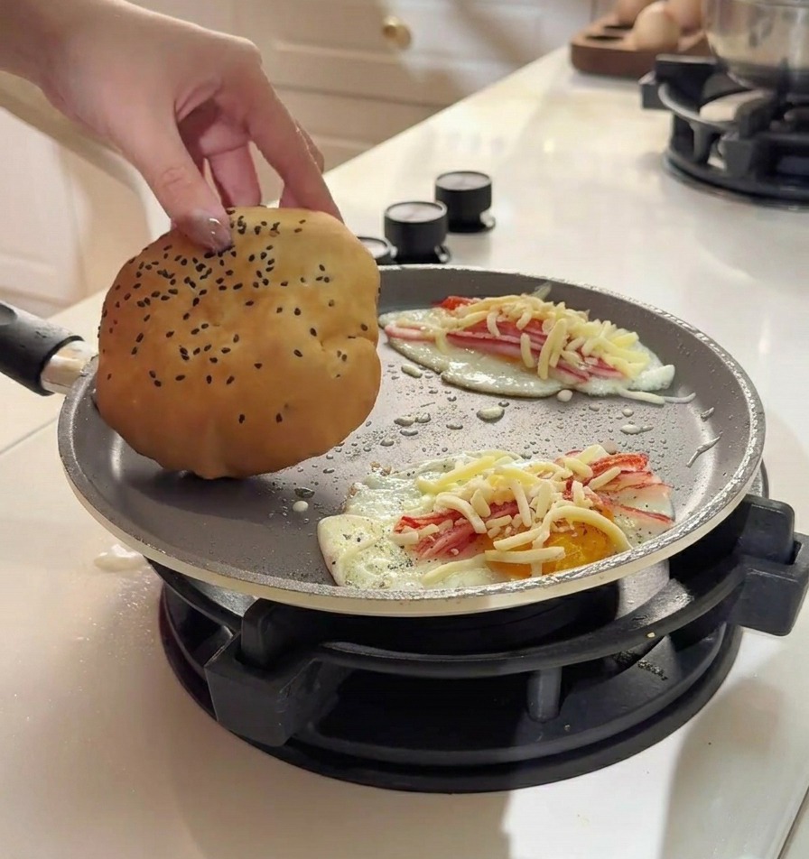팬 안의 계란과 치즈 위에 황금빛 버터 팬케이크 번을 올리는 모습