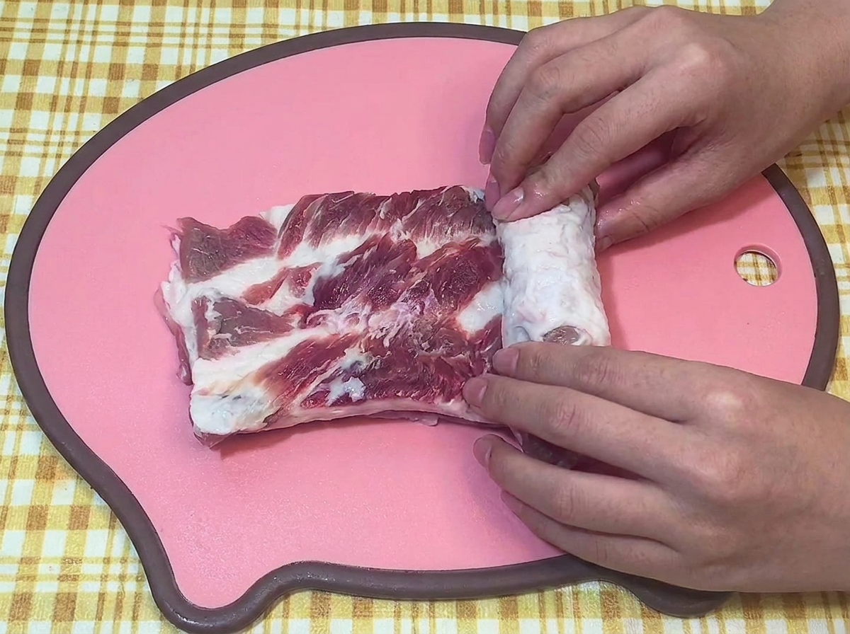 분홍색 도마 위에서 생삼겹살을 양손으로 단단하게 원통형으로 말고 있는 모습.
