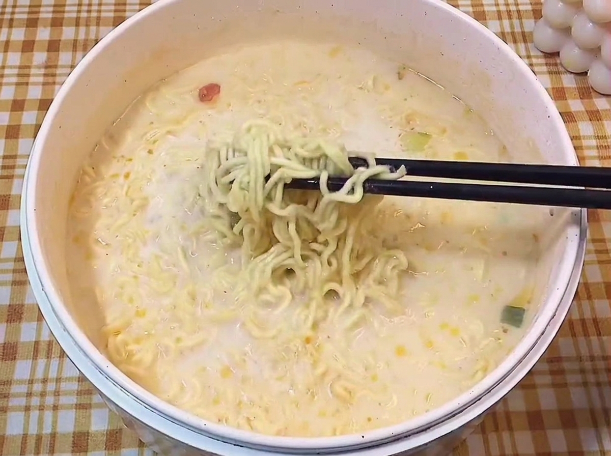 젓가락으로 뽀얀 국물 속에서 익은 라멘 면발을 들어 올리는 모습.