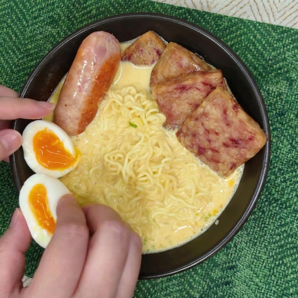 스팸 옆에 소시지와 노른자가 선명한 반숙란 반쪽 두 개를 정성스럽게 배치하는 모습