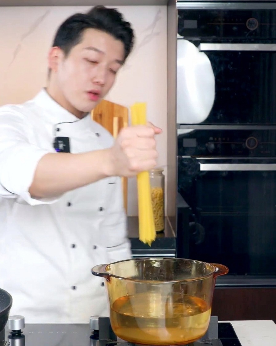 투명한 유리 냄비의 끓는 물에 스파게티면을 넣으려는 요리사의 모습.