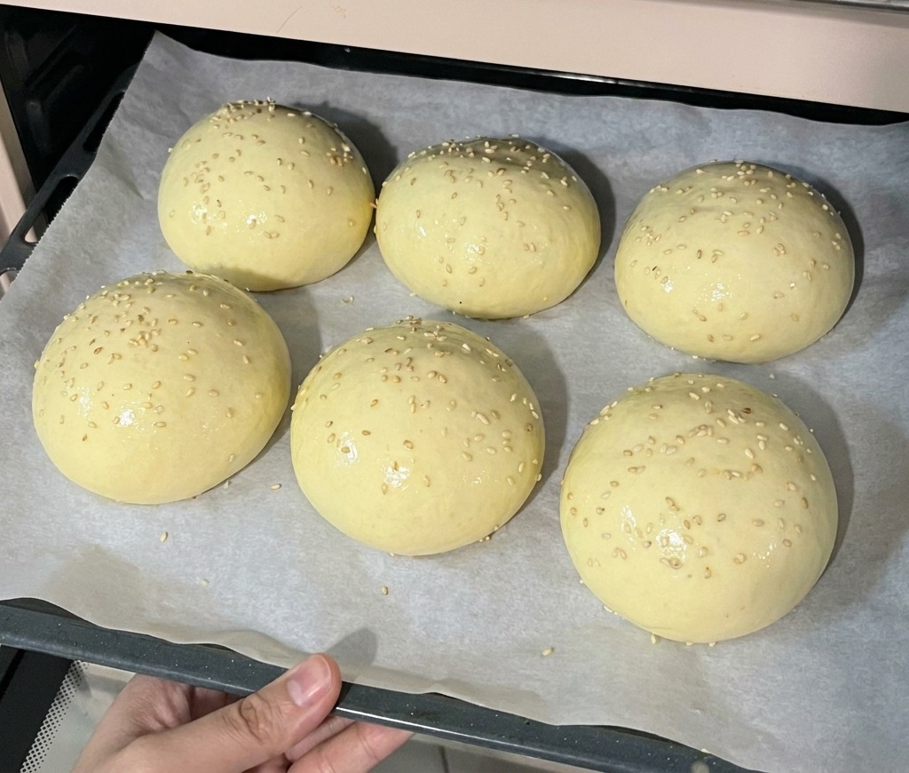 참깨가 뿌려진 버거 번 반죽을 예열된 오븐에 넣으려는 조리용 트레이