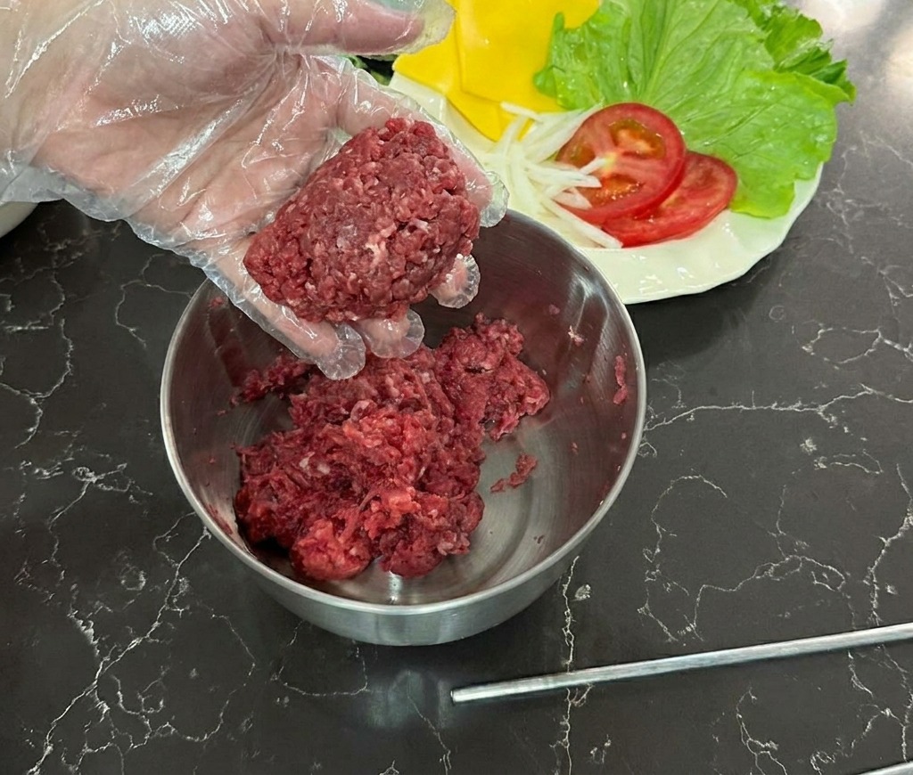비닐장갑을 낀 손으로 다진 소고기를 동그랗게 빚어 믹싱 볼 위에 들고 있는 모습
