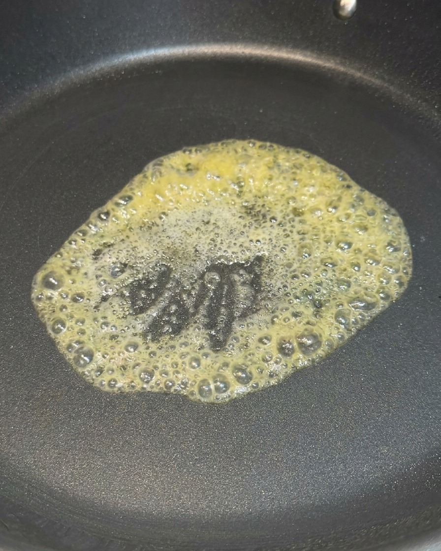 달궈진 검은색 코팅 팬 중앙에서 노란 버터 한 조각이 거품을 내며 녹고 있는 모습.