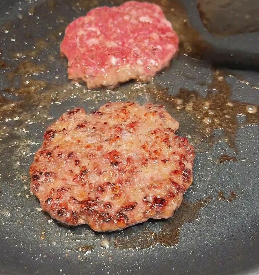 뒤집개로 소고기 패티를 뒤집어 잘 구워진 갈색 단면을 보여주는 모습.