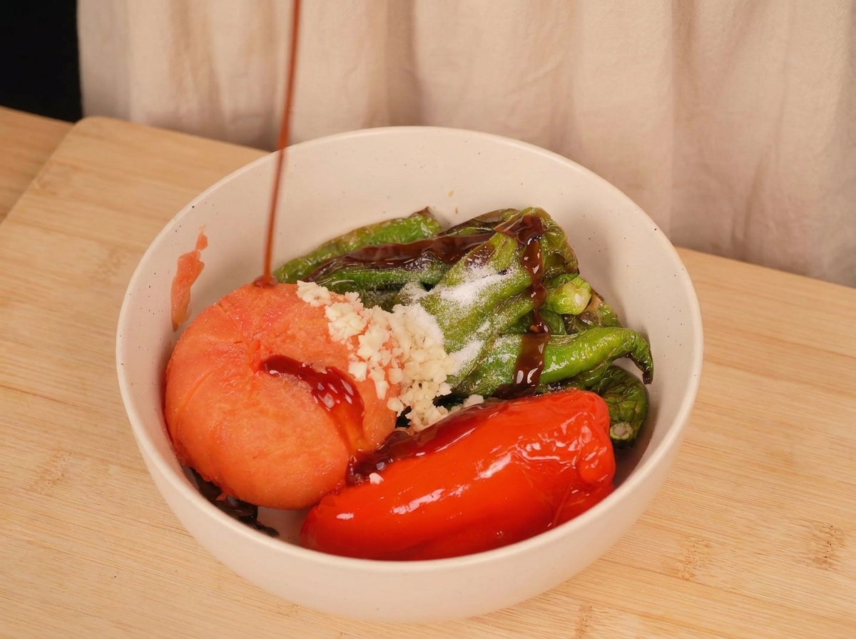 구운 고추, 토마토, 다진 마늘이 담긴 볼 위로 검은 굴소스를 뿌리는 모습.