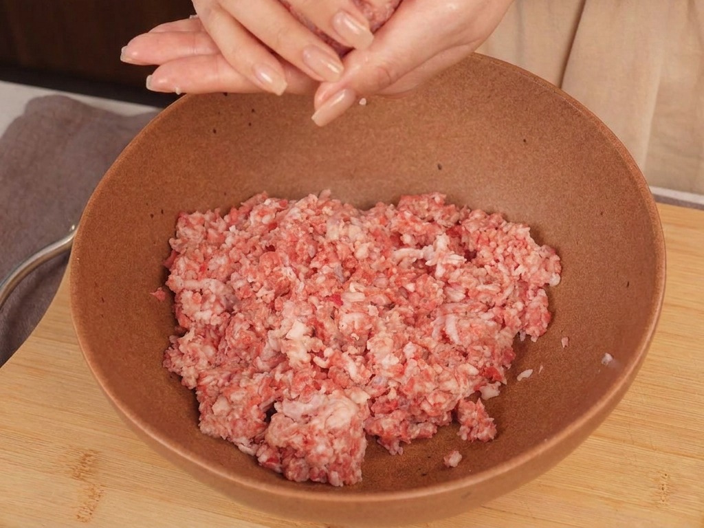볼 위에서 소고기 다짐육을 양손으로 굴려 둥근 공 모양으로 만드는 모습.