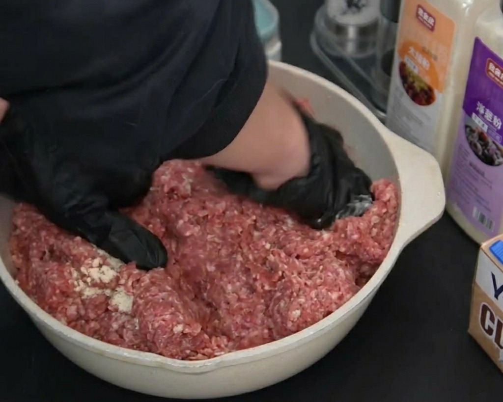 검은색 장갑을 끼고 양념이 뿌려진 소고기를 손으로 치대며 섞는 모습