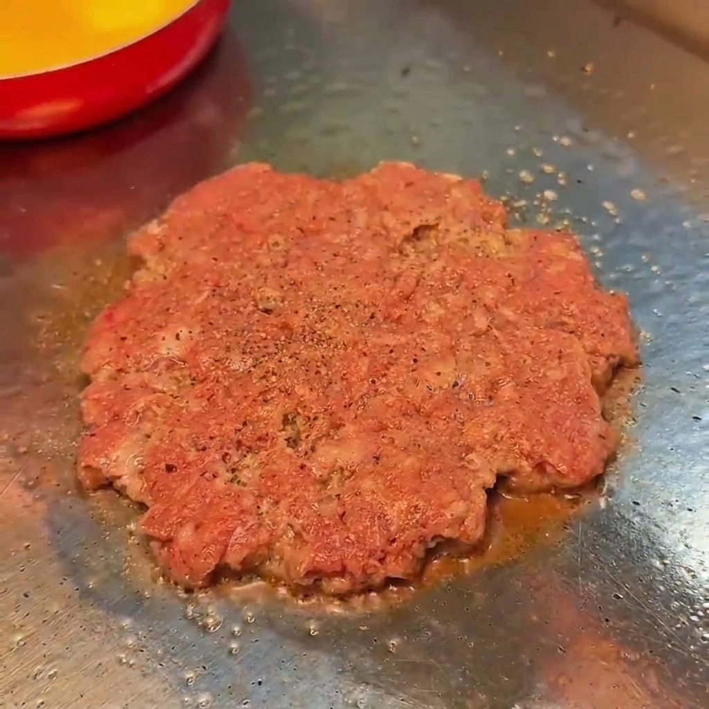 그릴 위에서 익어가는 소고기 패티에 소금과 후추를 뿌리는 모습
