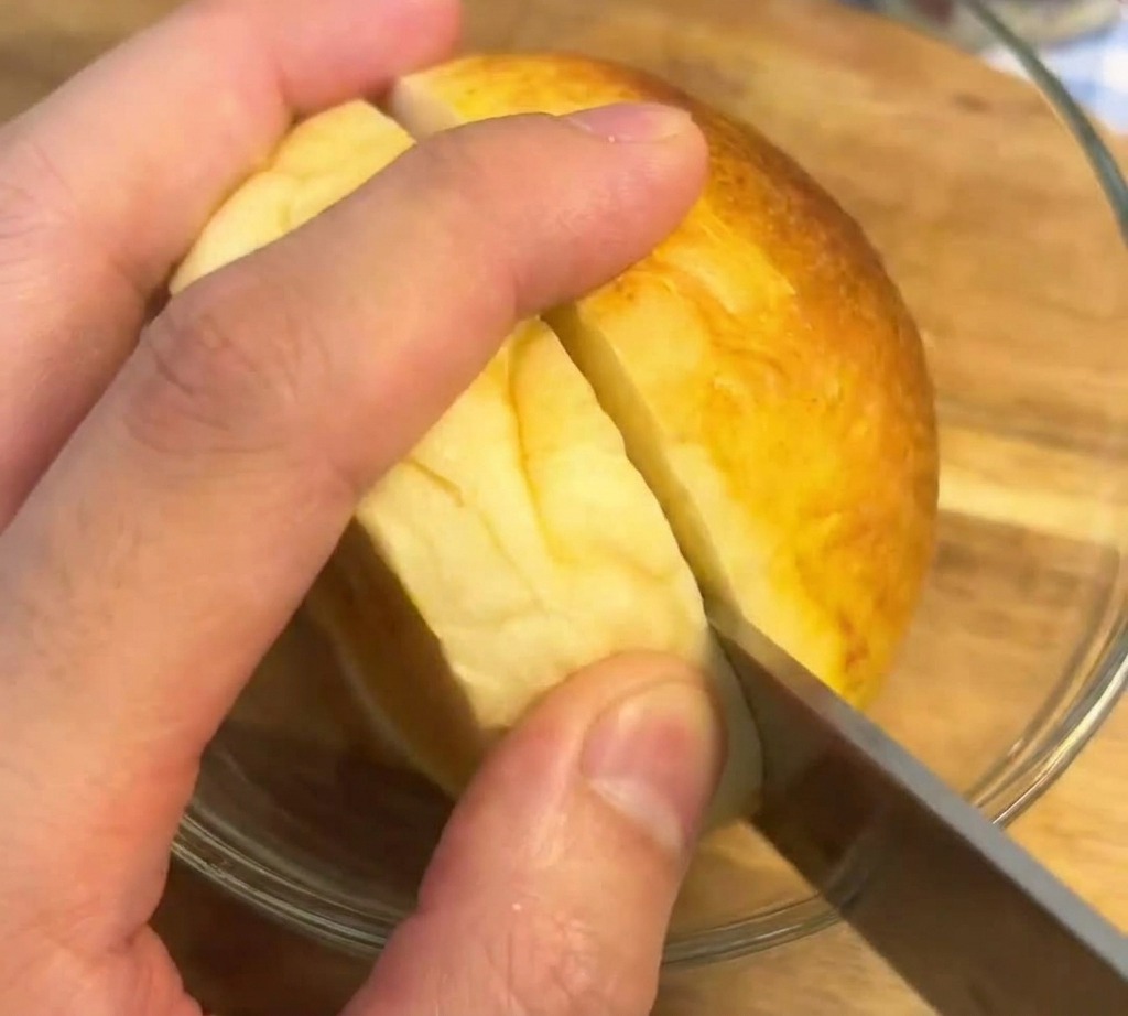 나무 도마 위에서 빵 칼을 이용해 노릇하게 구워진 버거 번을 가로로 자르는 모습.