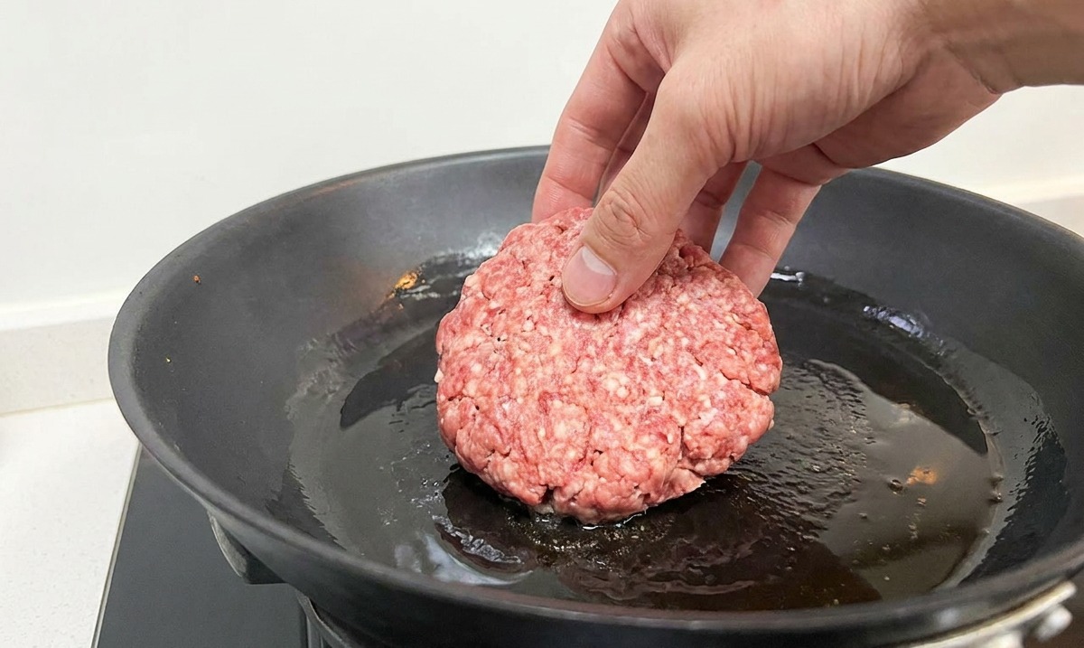 기름을 두른 뜨거운 무쇠 팬에 생소고기 패티를 올리는 모습.