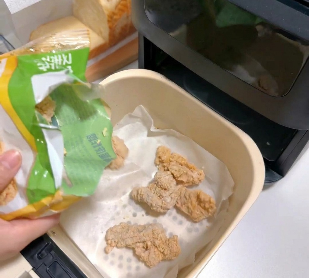 종이 호일을 깐 에어프라이어 바스켓에 냉동 치킨 조각들을 담는 모습.