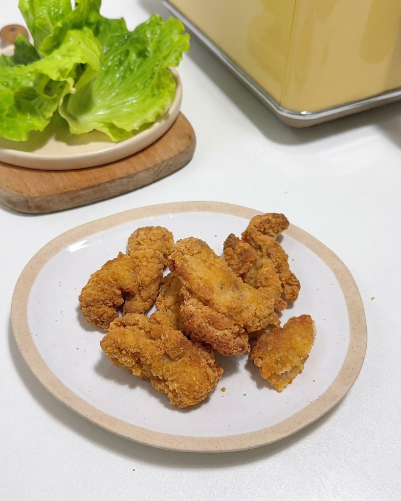 흰 접시 위에서 주방 가위로 바삭한 치킨을 자르는 모습.