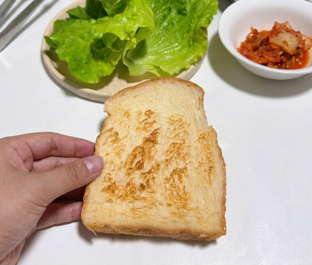 흰 조리대 위에서 구워진 식빵 한 장을 들고 있는 모습.