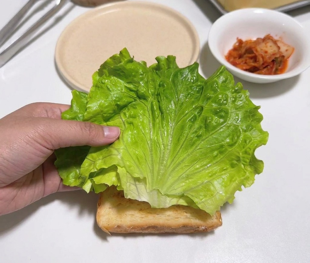 식빵 위에 초록색 상추 잎을 올리는 손.