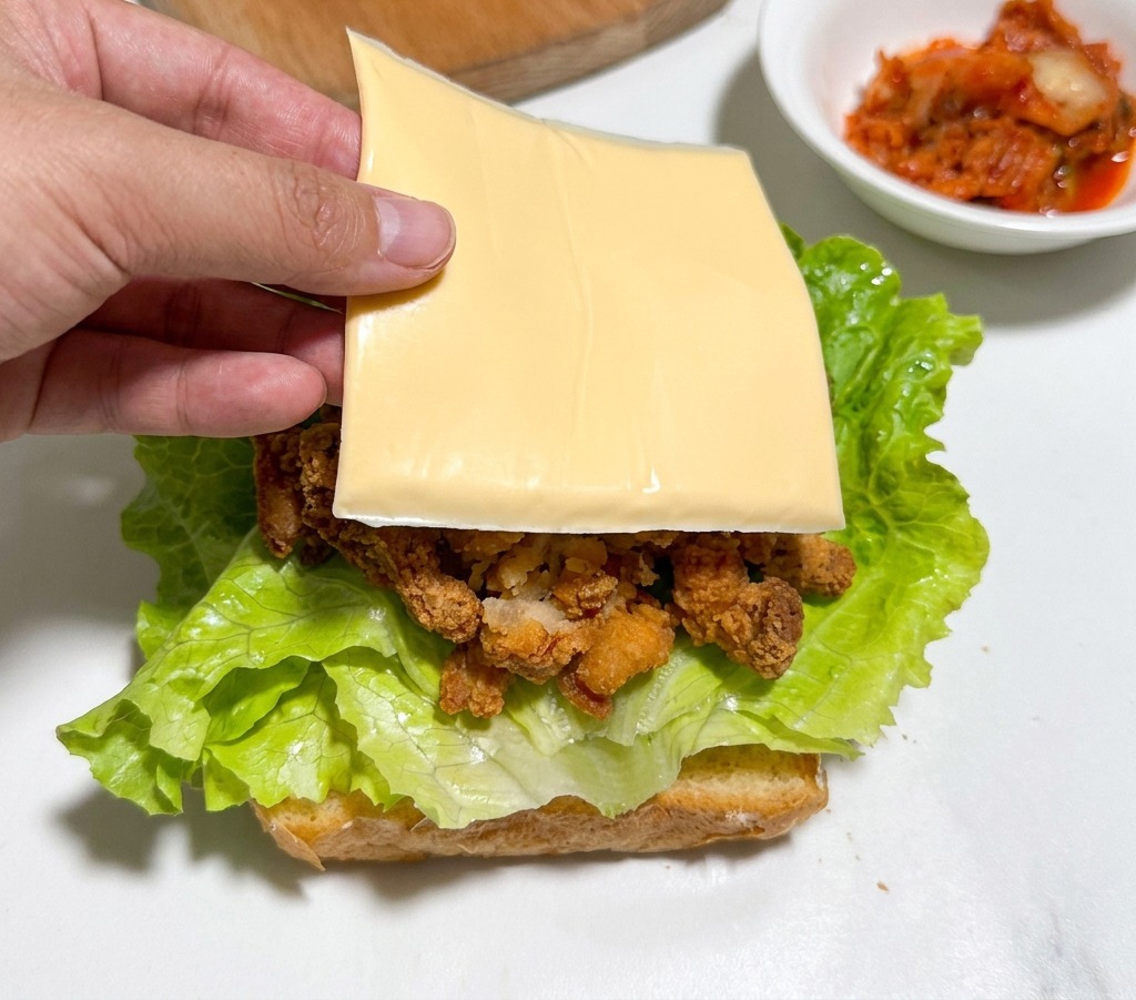 치킨과 소스 위에 노란 체다 치즈 한 장을 올리는 모습.
