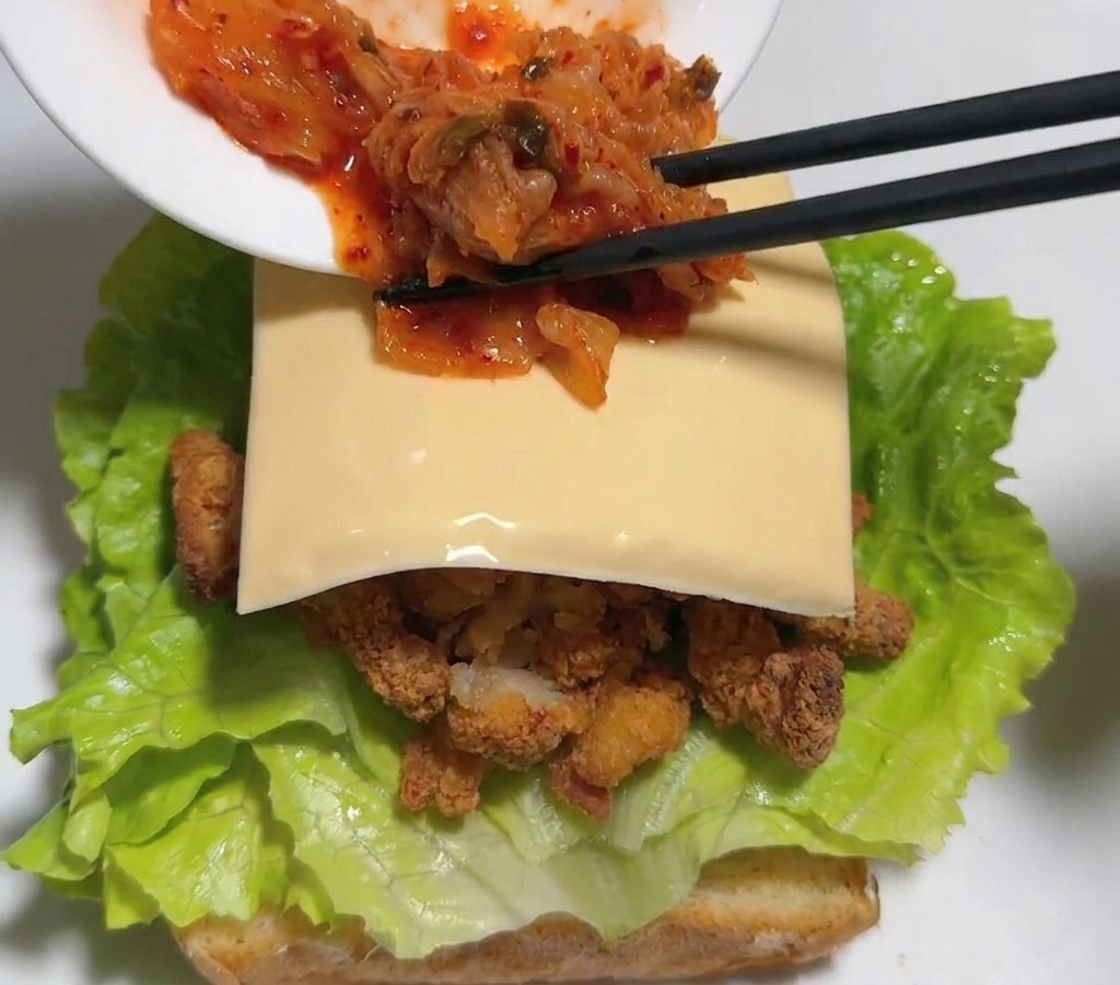 젓가락을 이용해 치즈 위에 붉은 배추김치를 올리는 모습.