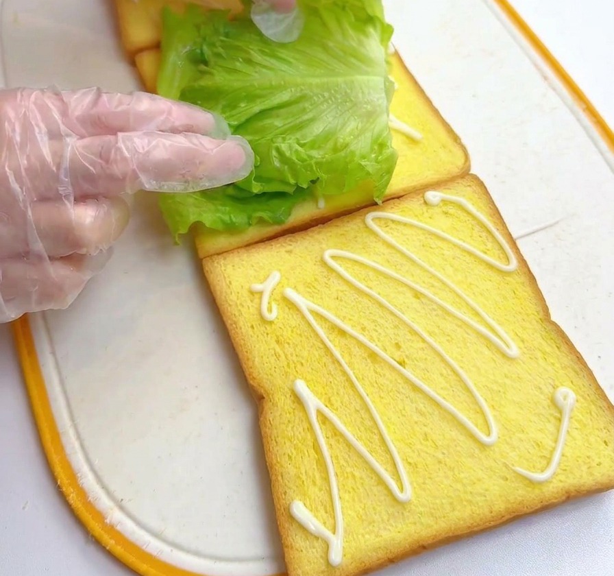 소스가 뿌려진 식빵 위에 신선한 청상추 잎을 올리는 모습