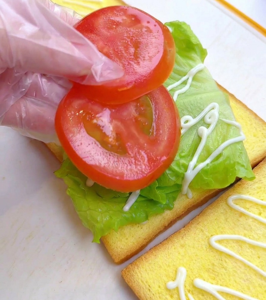 상추가 깔린 식빵 위에 슬라이스한 토마토 두 조각을 올리는 모습