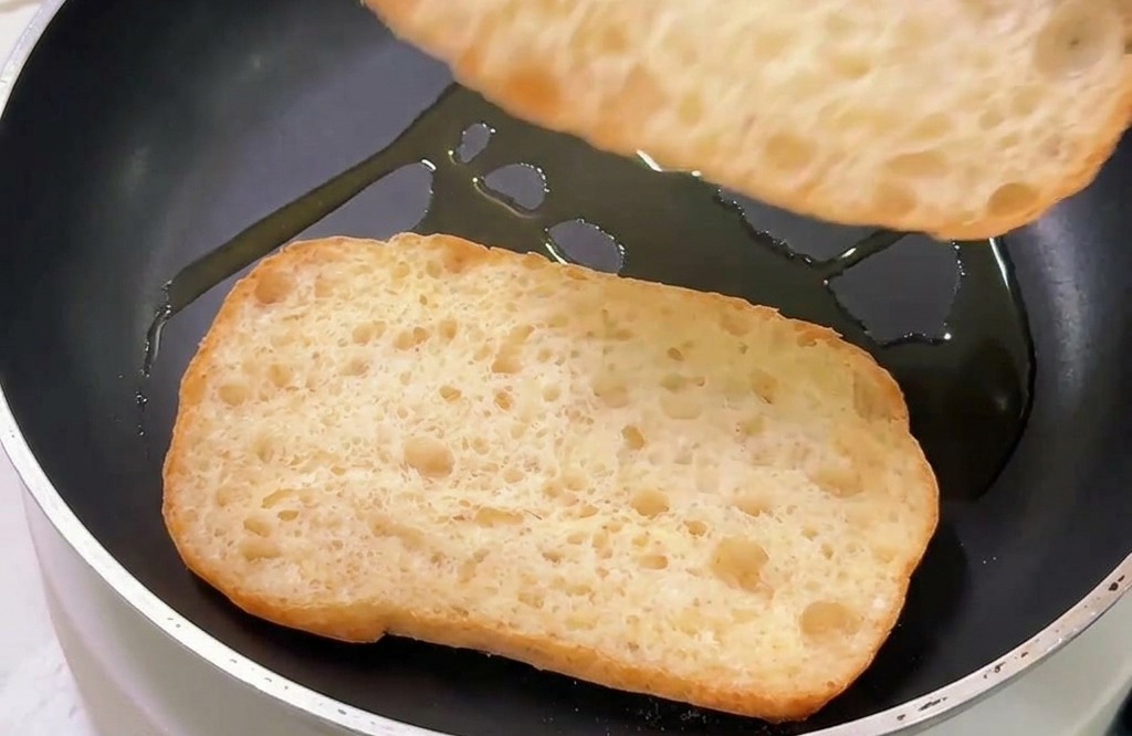 기름을 살짝 두른 팬에 치아바타의 자른 단면이 바닥을 향하도록 올려 굽는 모습.
