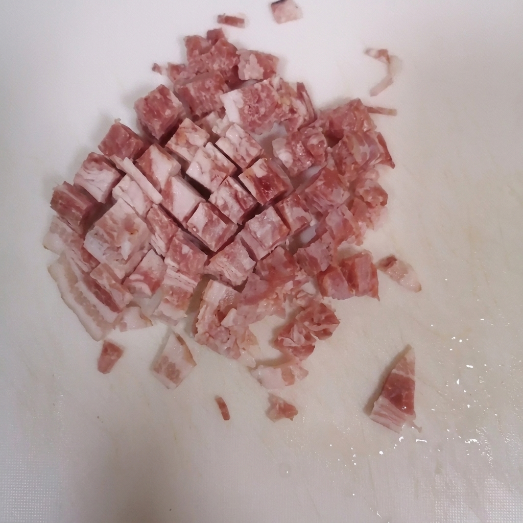 깨끗한 흰색 도마 위에서 베이컨을 작게 깍둑썰기하는 모습.