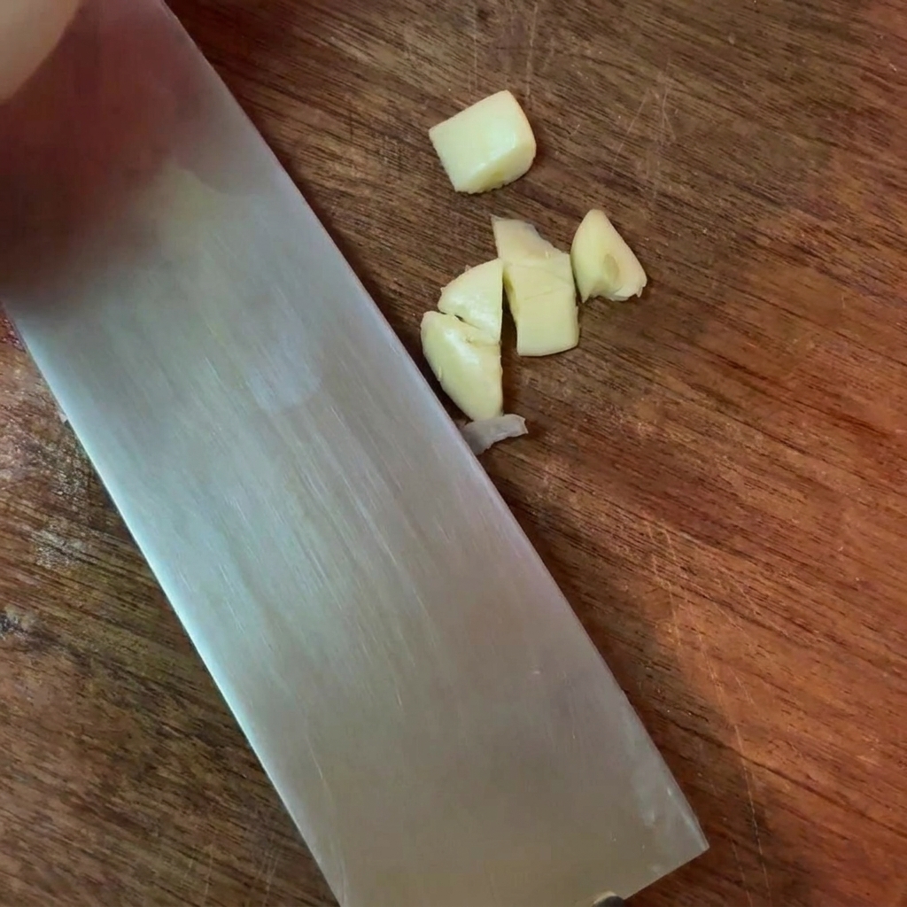 도마 위에서 칼로 마늘을 잘게 다지는 모습.