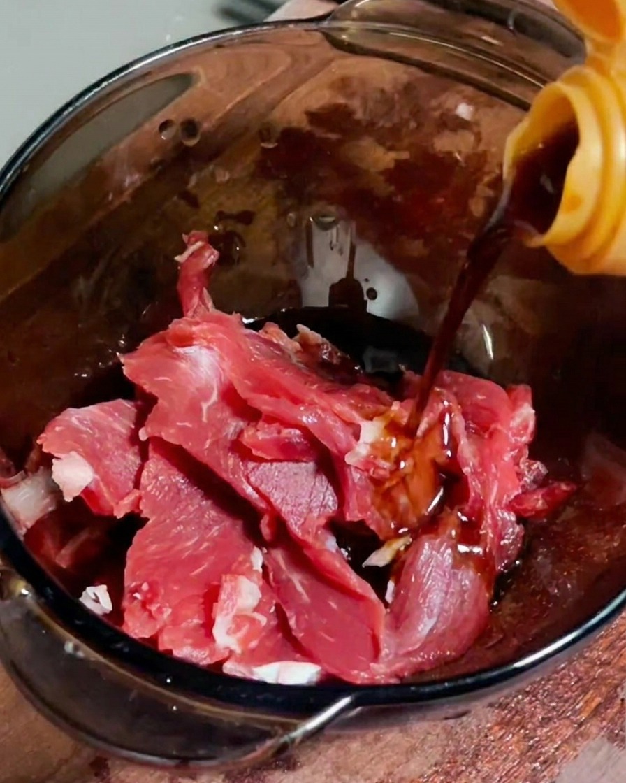 유리 볼에 담긴 생소고기에 간장을 붓는 모습.