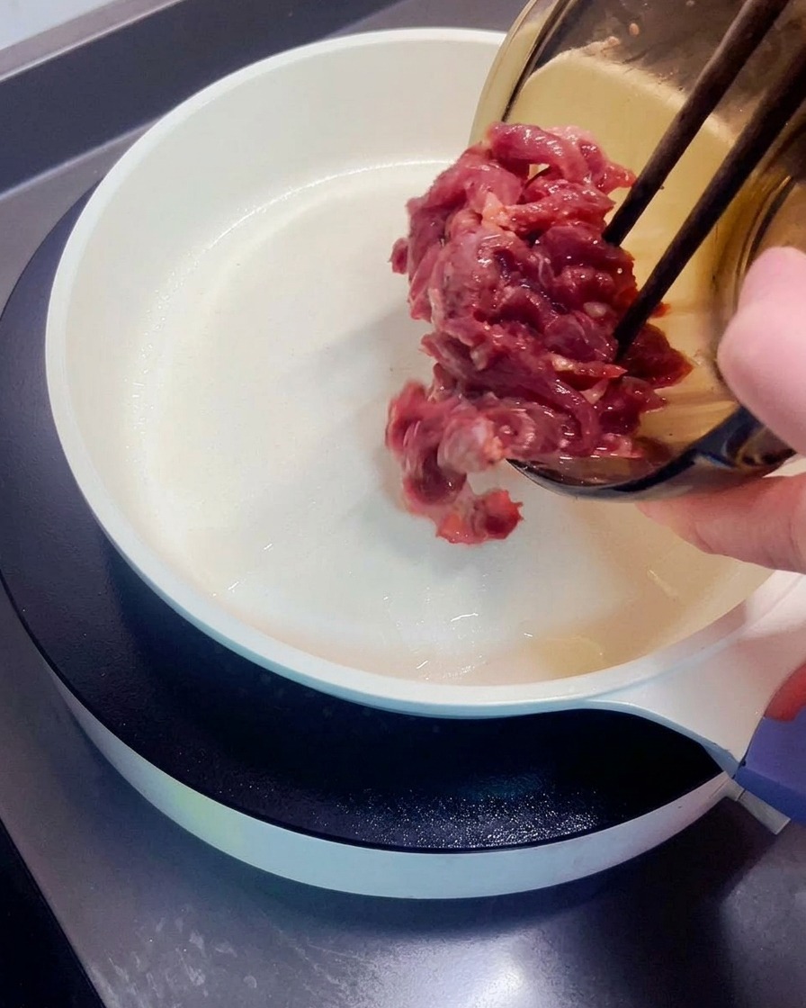 달궈진 흰색 팬에 재워둔 소고기를 올리는 모습.
