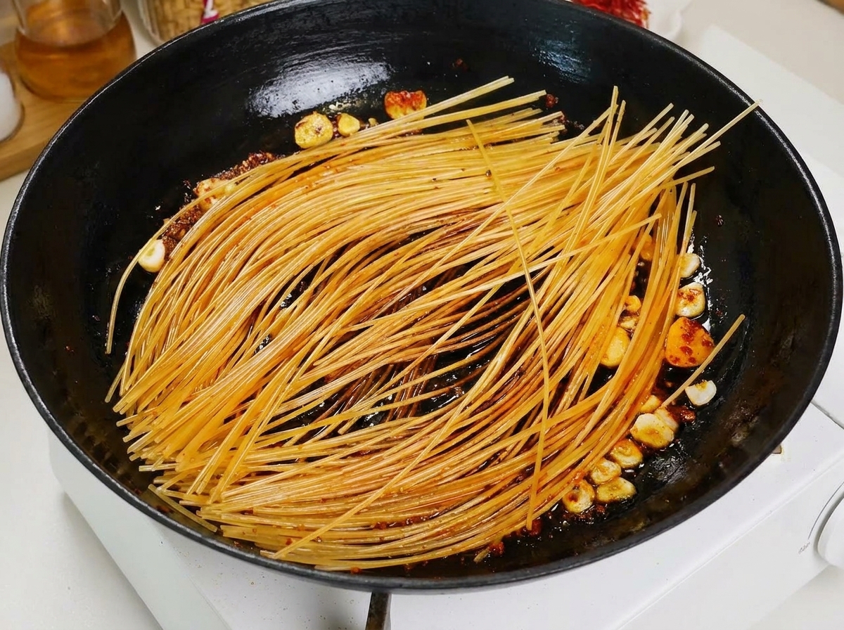 검은 팬의 구워진 스파게티 위로 국자로 빨간 토마토 육수를 붓는 모습.