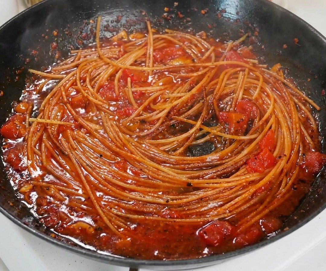 검은 팬 안에서 진한 토마토 소스에 버무려진 익은 스파게티의 근접 촬영.