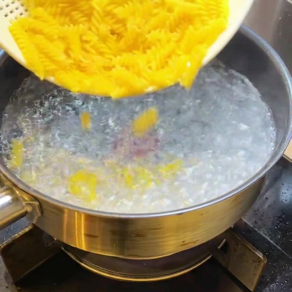 건조된 푸실리 파스타를 끓는 물이 든 냄비에 쏟아 넣는 모습.