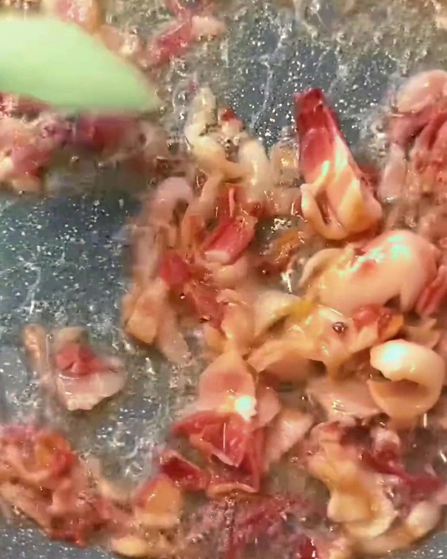 팬 안에서 바삭하게 구워진 베이컨과 진한 붉은색 토마토 소스가 어우러져 끓고 있는 모습.