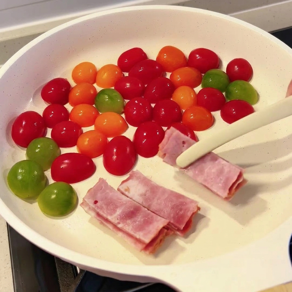집게를 사용하여 베이컨 조각을 방울토마토가 담긴 팬에 넣는 모습.