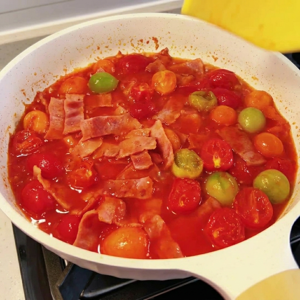 토마토 베이컨 소스 위로 노란 슬라이스 치즈가 녹아드는 모습.