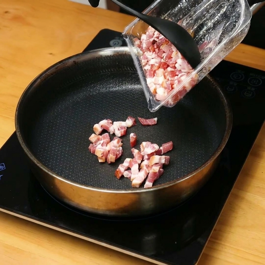 달궈진 팬에서 잘게 썬 베이컨이 노릇노릇하게 구워지며 기름이 나오는 모습.