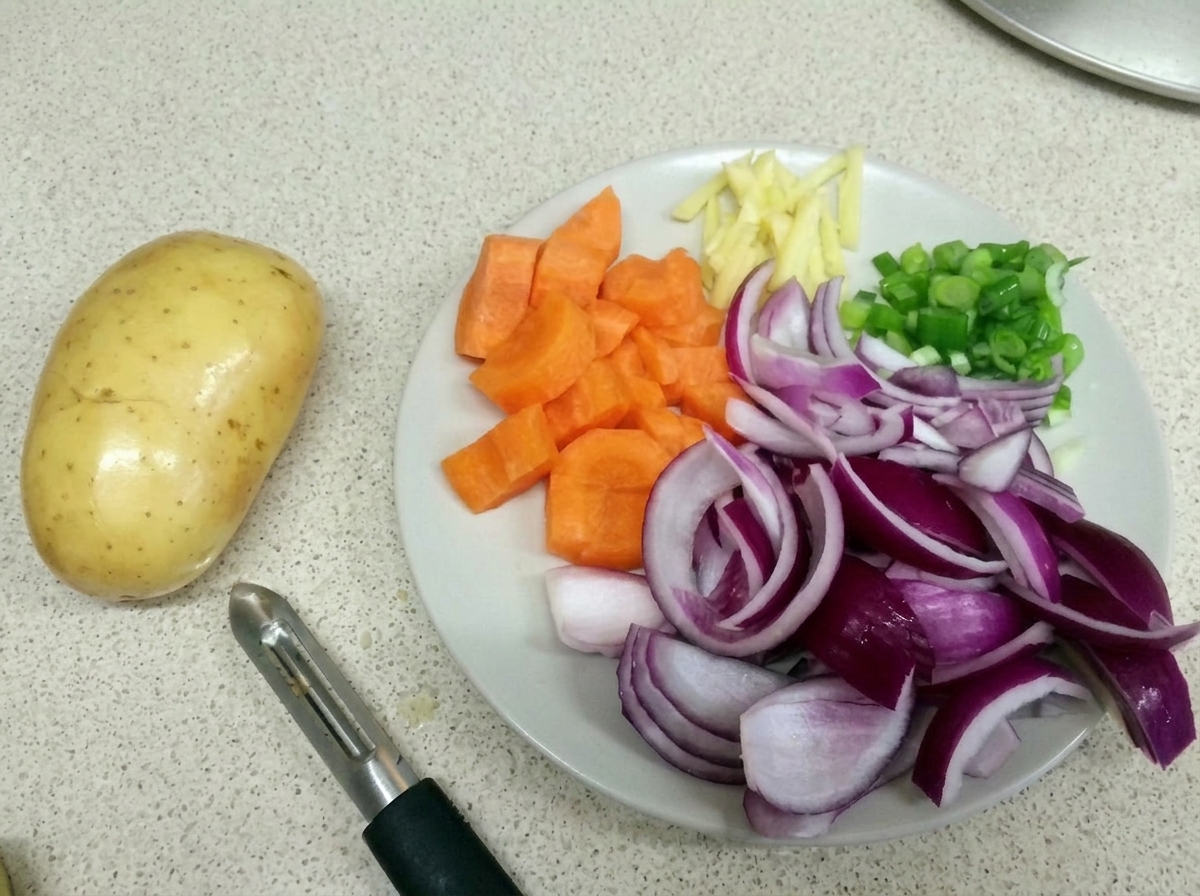 도마 위에 채 썬 당근, 적양파, 생강, 대파가 놓여 있고 옆에 감자와 감자칼이 있는 모습.