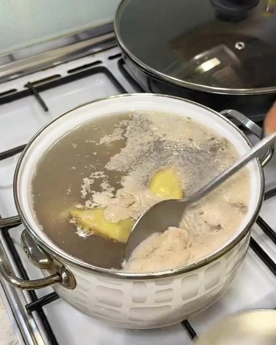 숟가락으로 끓는 물 위의 회색 거품을 걷어내는 모습.