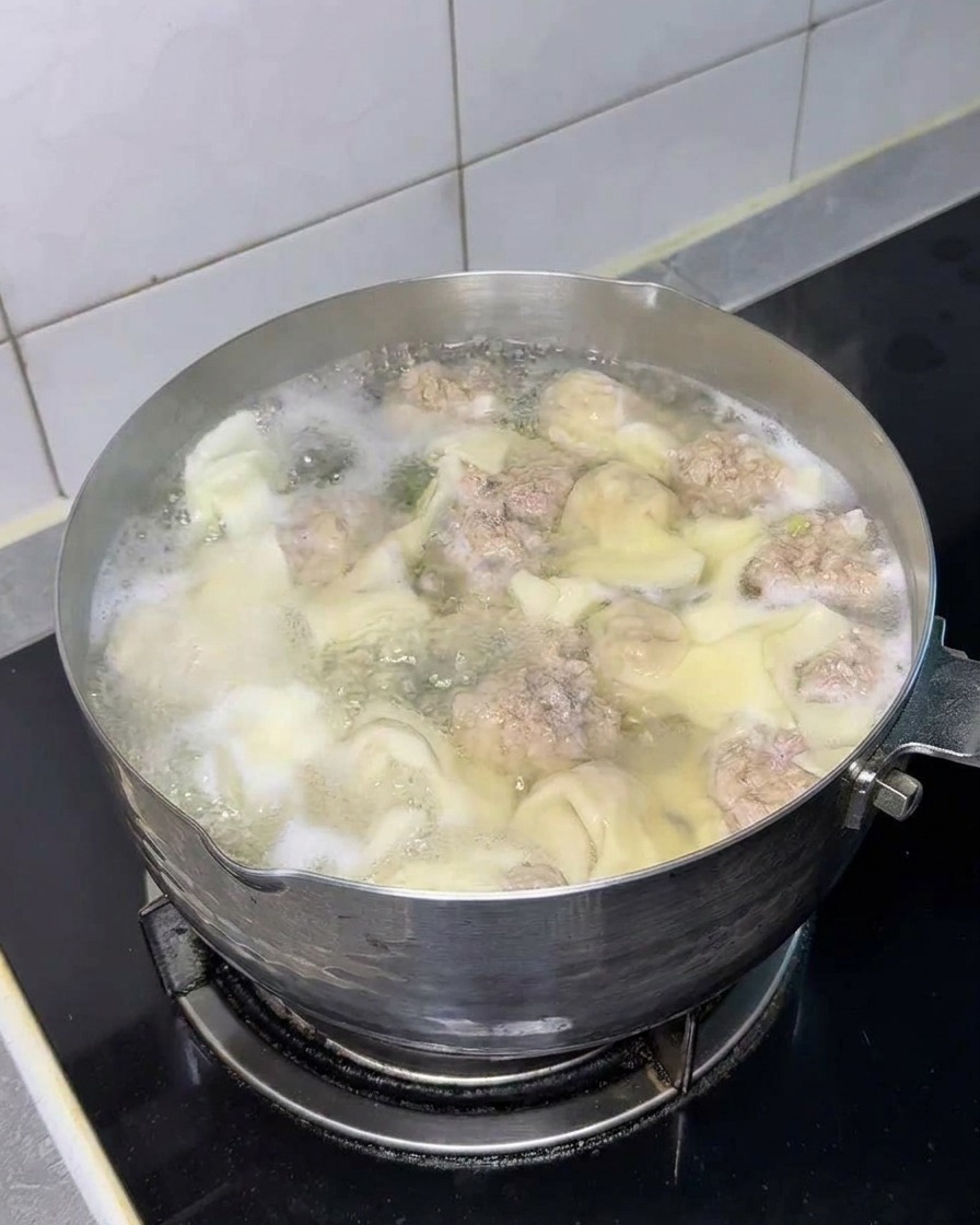 완탕과 미트볼이 있는 냄비에 건조된 네모난 라면 사리가 담긴 모습.