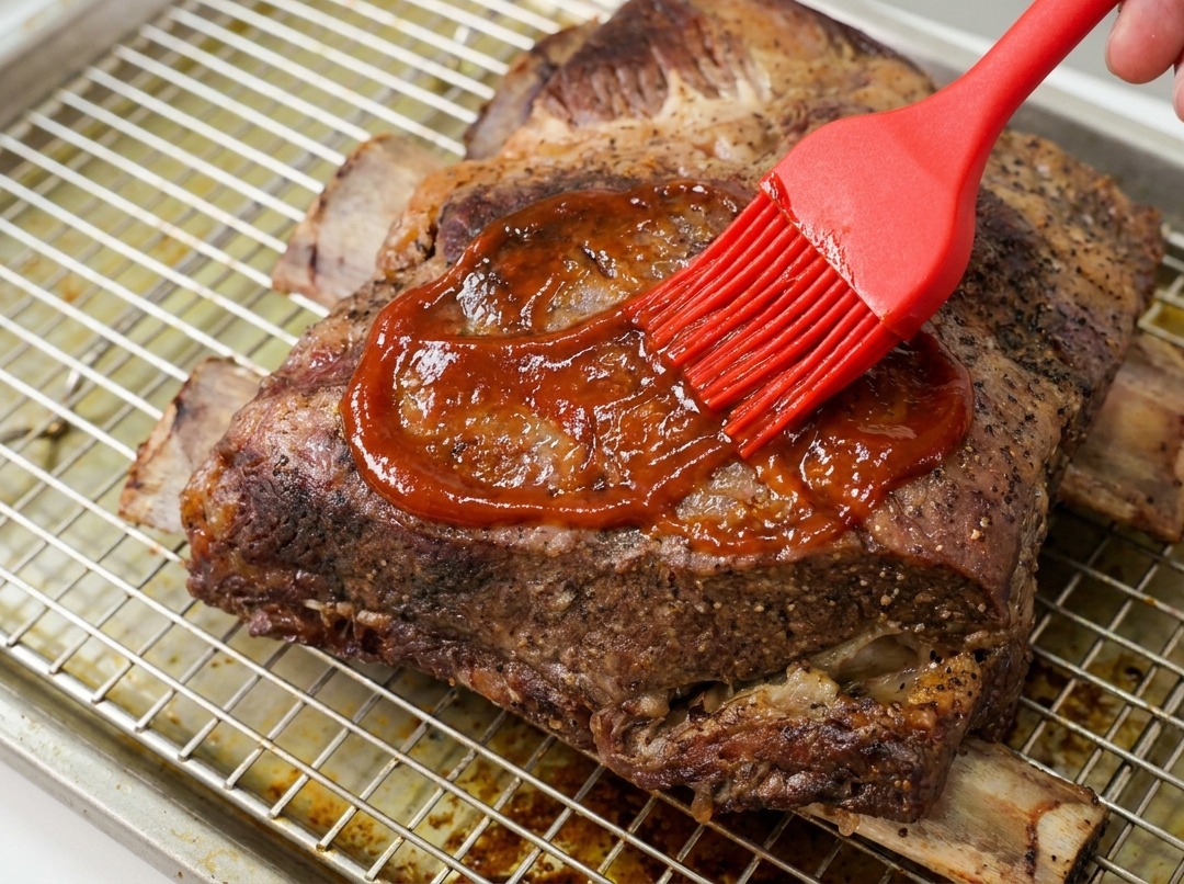 실리콘 브러시로 소갈비 덩어리 표면에 윤기 나는 BBQ 소스를 듬뿍 바르는 모습.