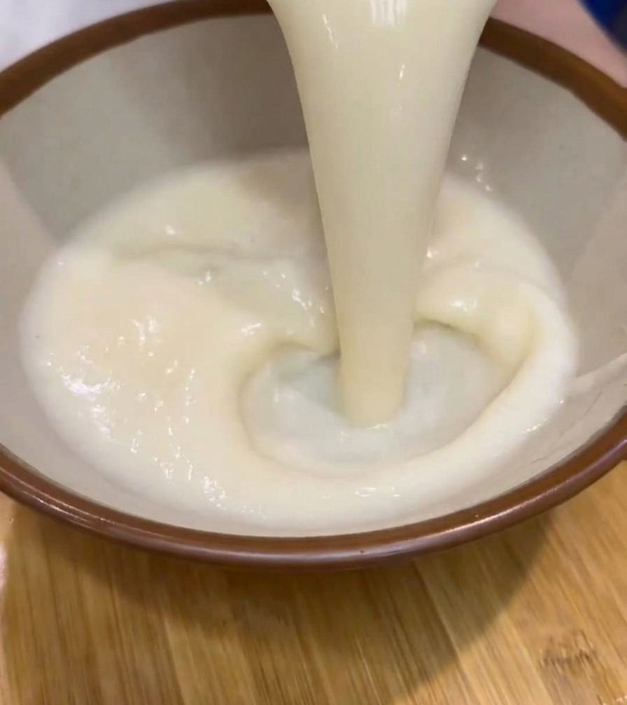 진한 크림색의 뜨거운 라멘 육수를 갈색 테두리가 있는 도자기 그릇에 붓는 모습.
