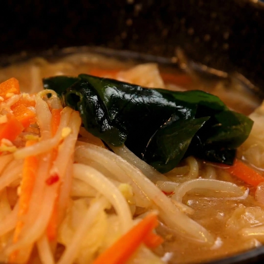 삶아진 면을 건져 준비된 미소 국물 그릇에 옮겨 담는 모습.