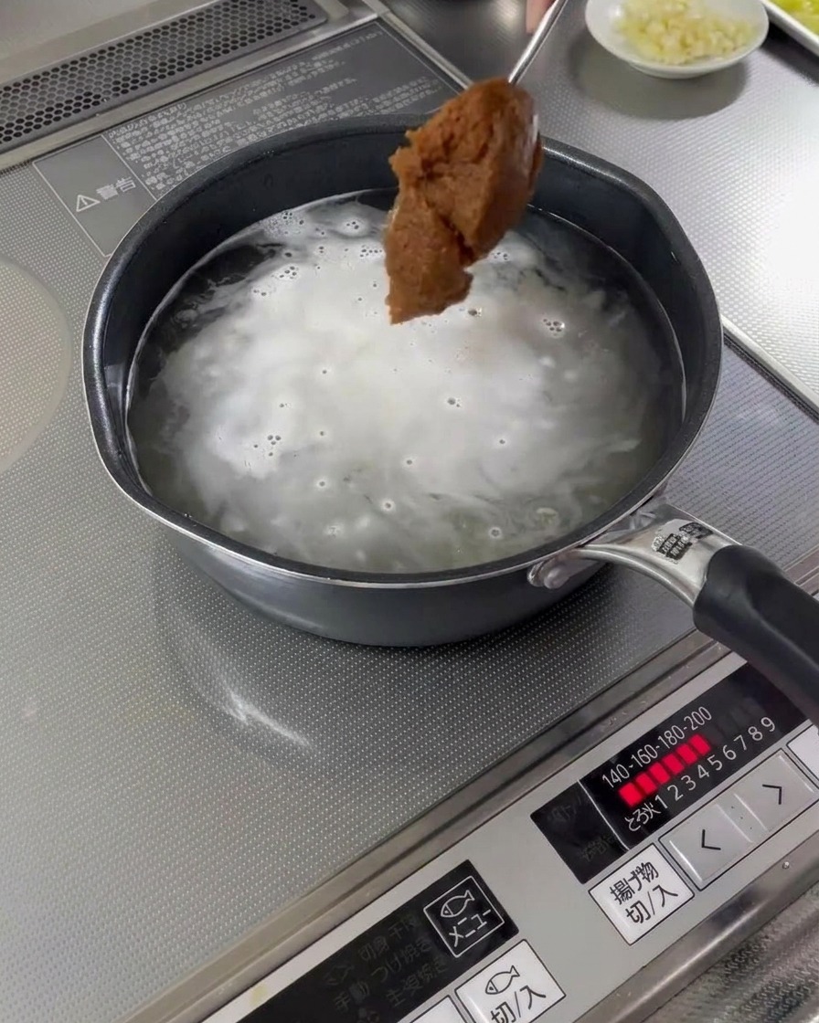 끓는 육수가 담긴 냄비에 숟가락으로 미소 된장을 추가하는 모습.