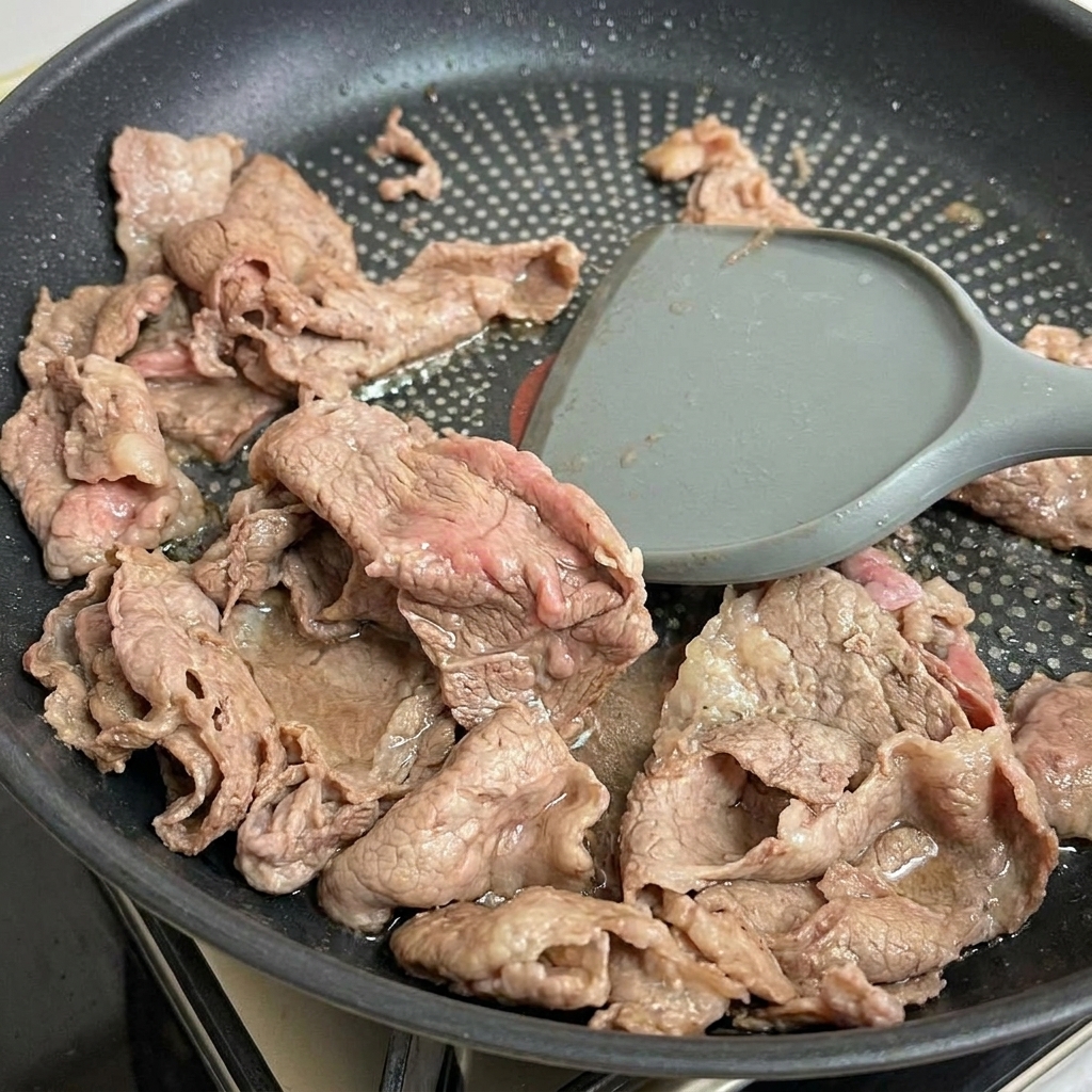 뒤집개로 살짝 익은 소고기를 팬에서 건져내는 모습.