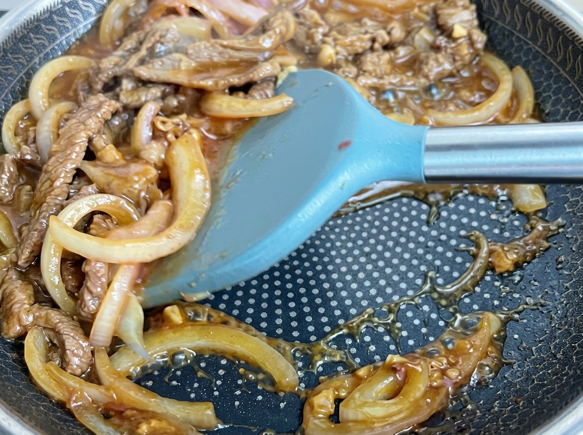 팬에서 소스가 끓으며 고기와 양파가 졸여지는 모습.