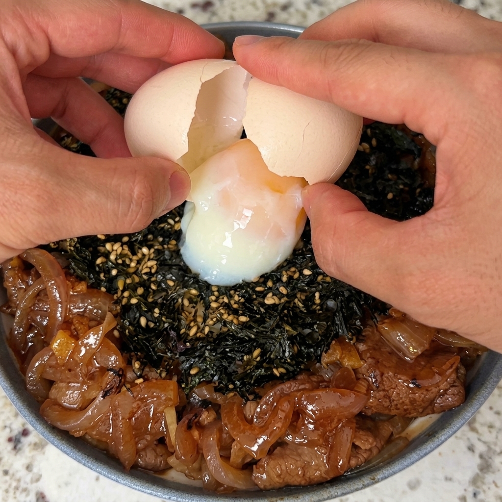 완성된 덮밥 중앙에 온천 달걀을 깨어 올리는 모습.